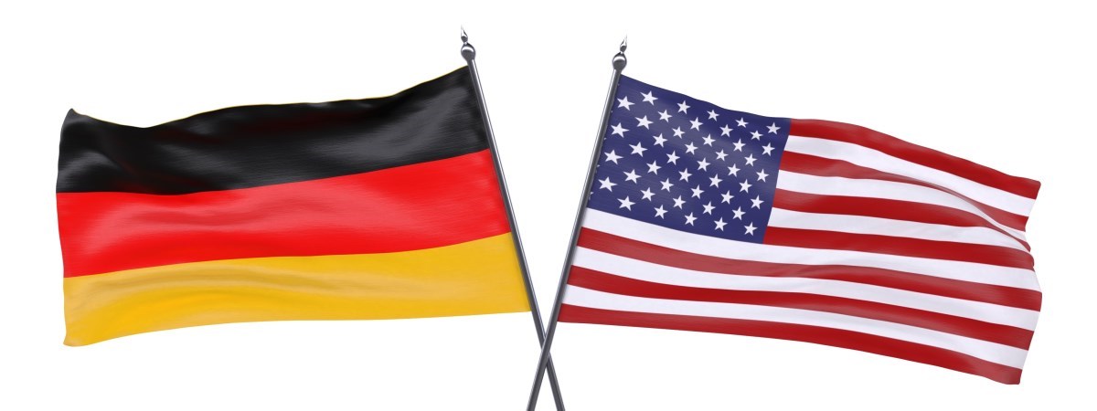 Eine amerikanische Flagge und eine deutsche Flagge. Die Fahnenhalterungen kreuzen sich.